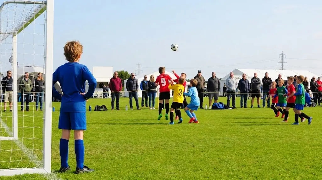 Youth soccer players jumping for a header during an outdoor game with parents watching from the sidelines, representing a standard environment for recording family sports with the ORDRO XV80.