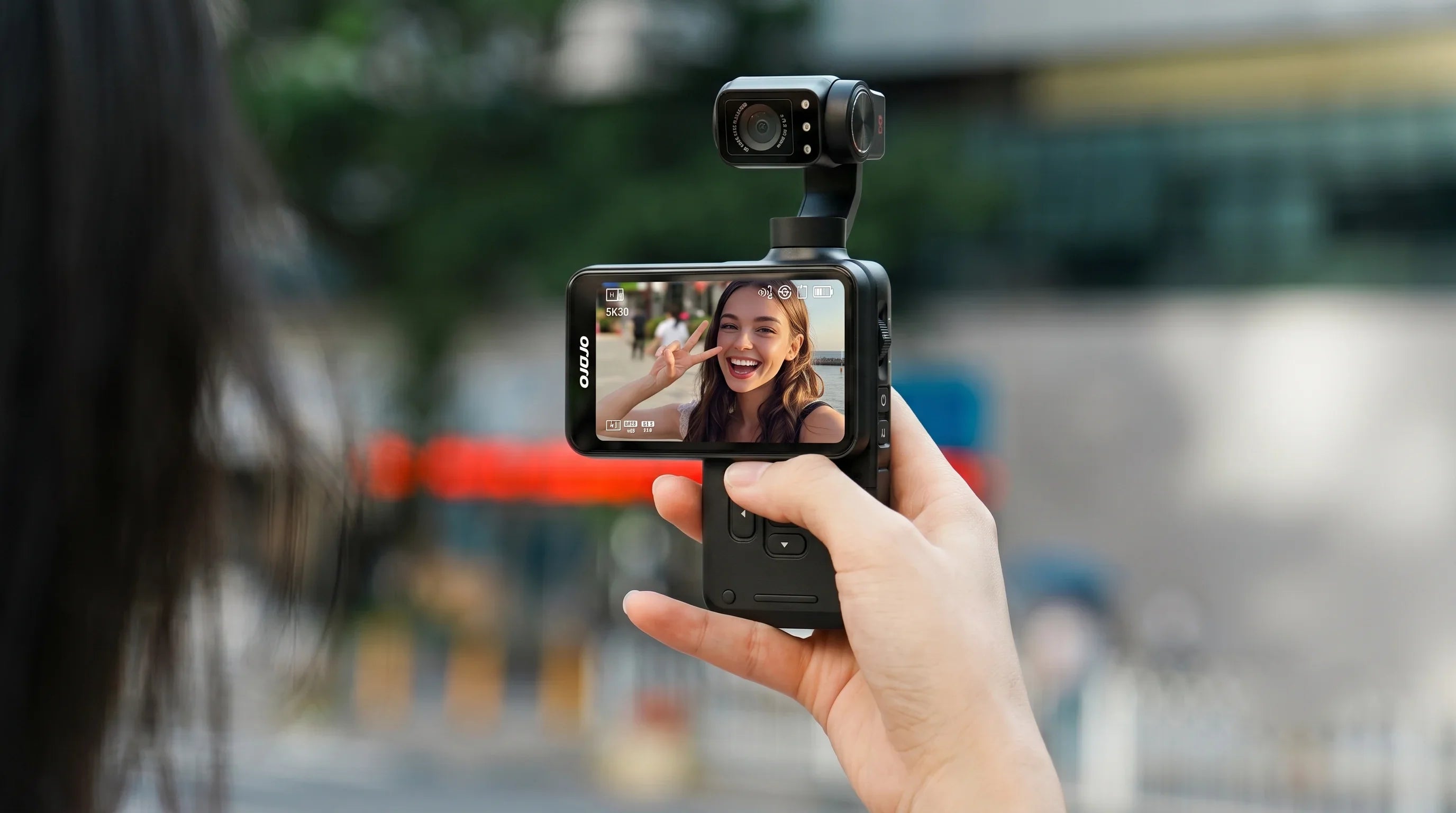 Solo traveler vlogging on a city street with the ORDRO Pocket M5, showing its 3-axis gimbal stabilization and 3.5-inch touchscreen.